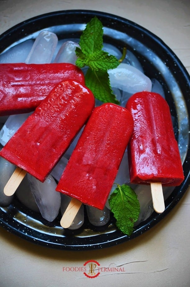 Strawberry popsicles kept on ice cubes on a black plate