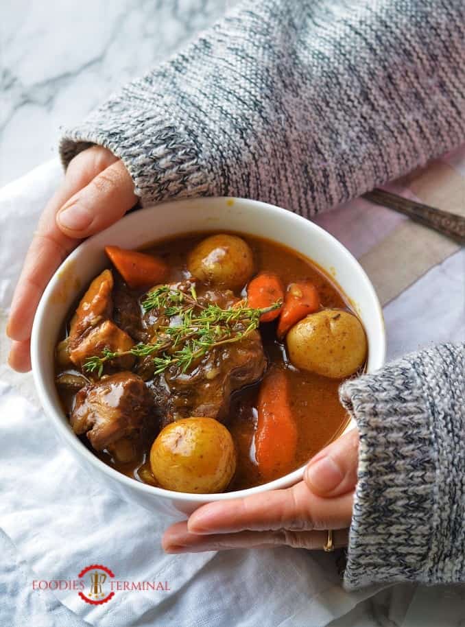 Hands holding a bowl of lamb stew cooked in Instant Pot