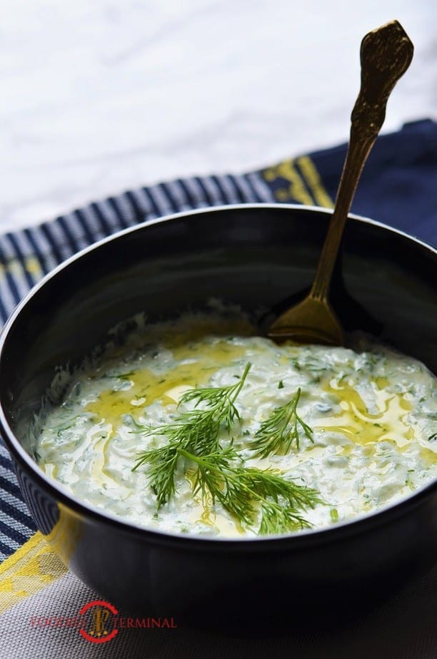 Tzatziki recipe garnished with dill & olive oil in black bowl with gold spoon
