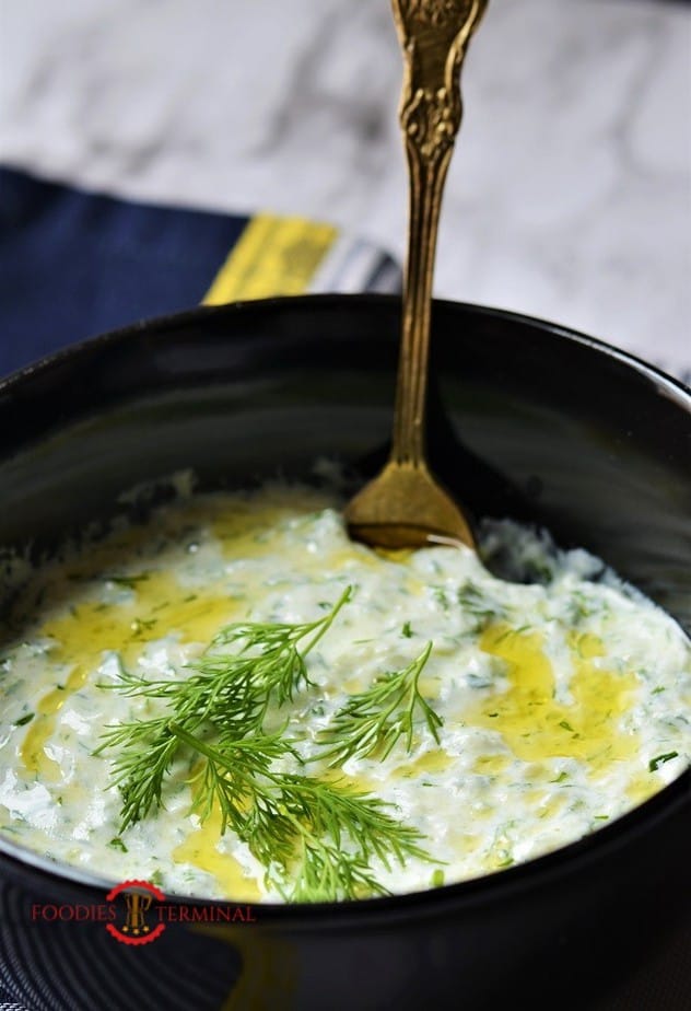 Greek Tzatziki Sauce garnished with dill in a black bowl with a gold spoon