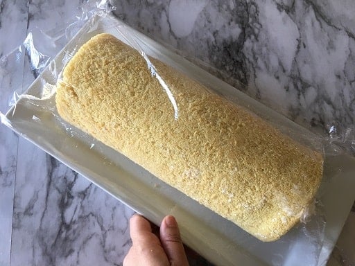 Vanilla Swiss Roll Cake recipe with cling film on a plate