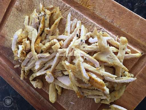 Thin strips of pan seared chicken on a wood board