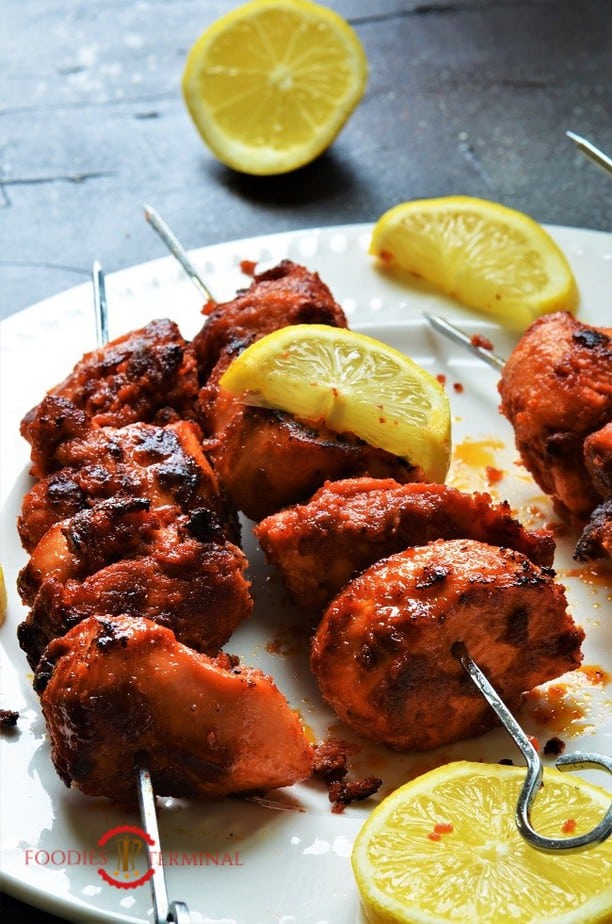 Tender juicy chicken boti kabab on a white plate with lemon wedges