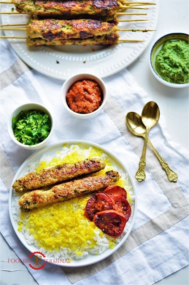 Chicken seekh kabab on a plate with rice, tomatoes & chutneys