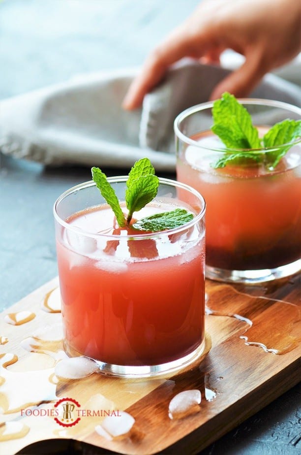 Gorgeous pink Kokum Sharbat in two glasses on a wood board with broken ice cubes all around