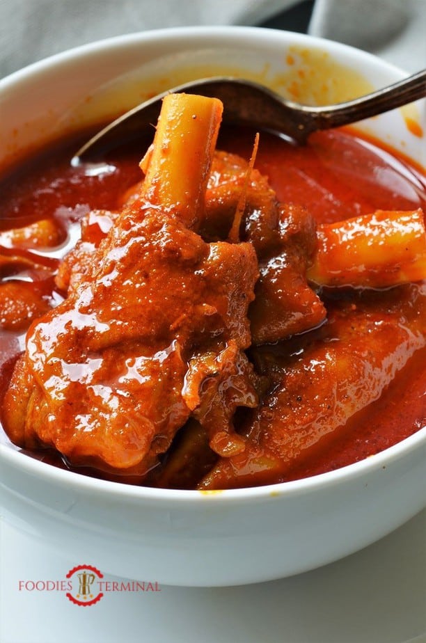 Mutton Paya with goat trotters in a red curyy sauce in a white bowl