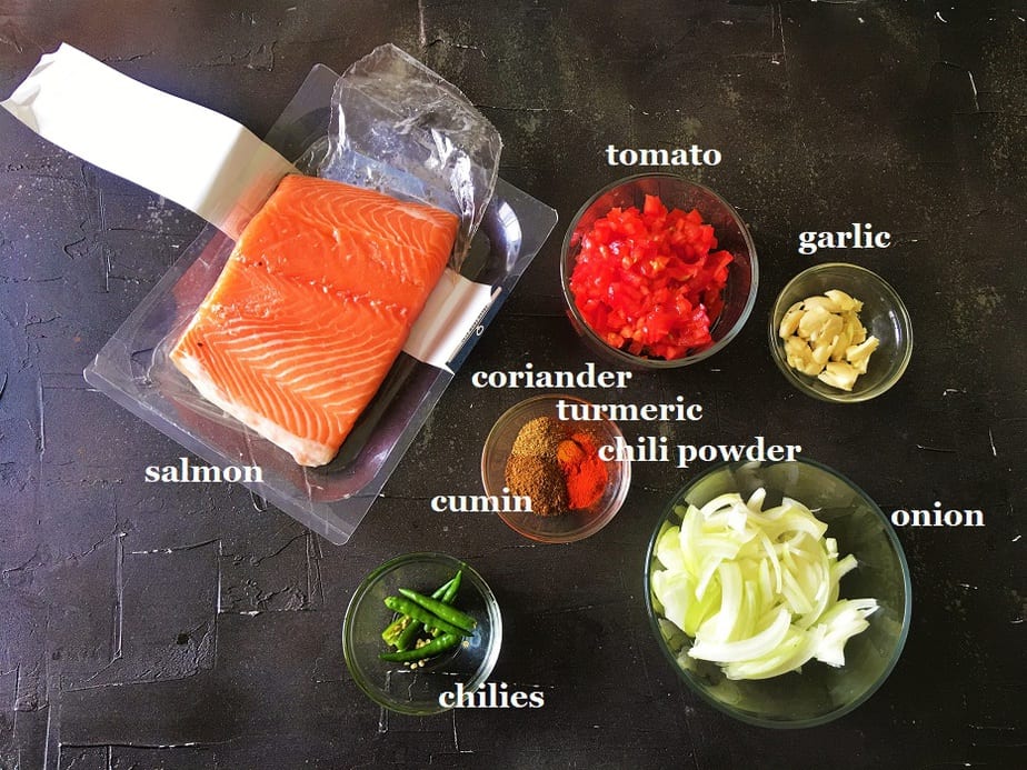 Ingredients for easy Salmon curry in various bowls on a black surface