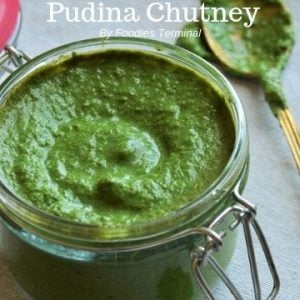 Mint coriander chutney in a glass jar with aspoon beside