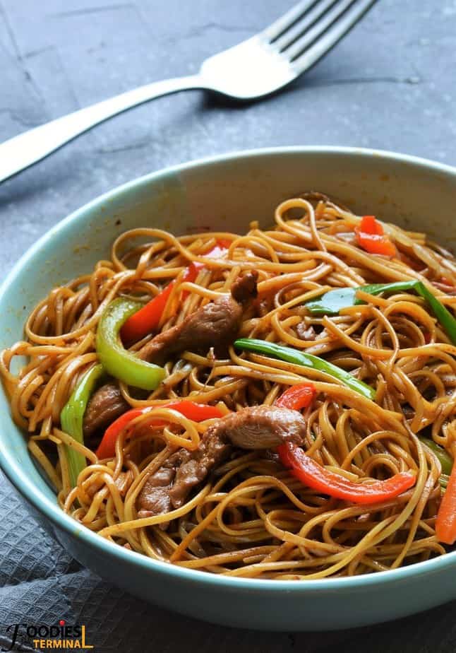 P. F. Chang style chicken lo mein in a pale blue bowl with a fork by the side