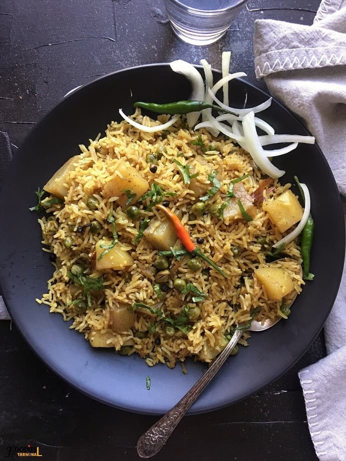 Instant Pot aloo mutter pulao served on a black plate with chilies & onion