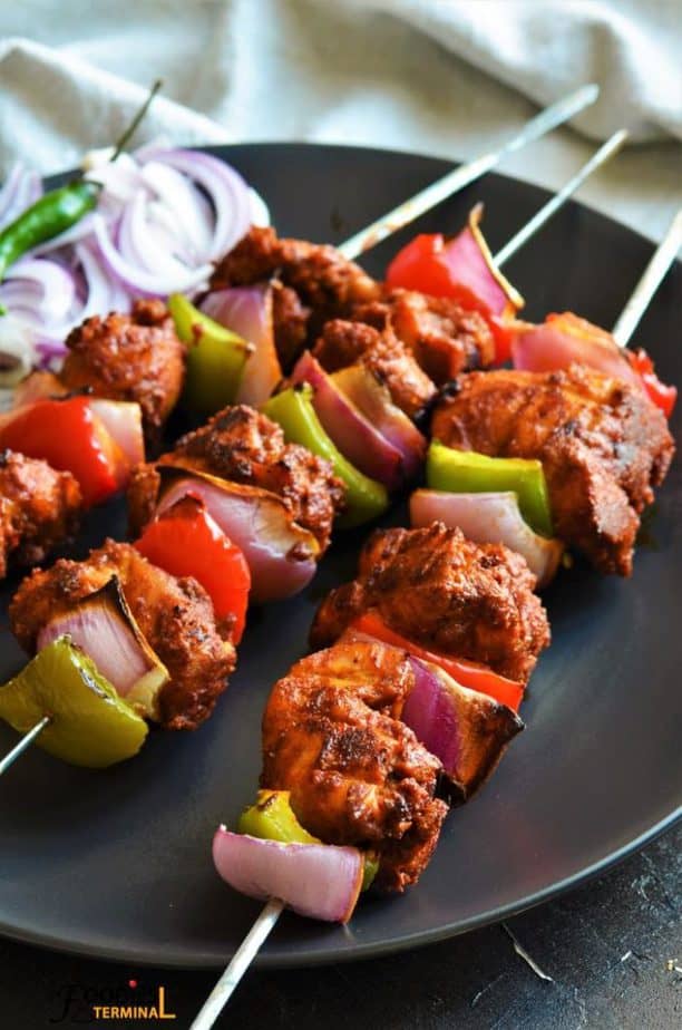 Chicken Tikka in oven on a black plate in skewers