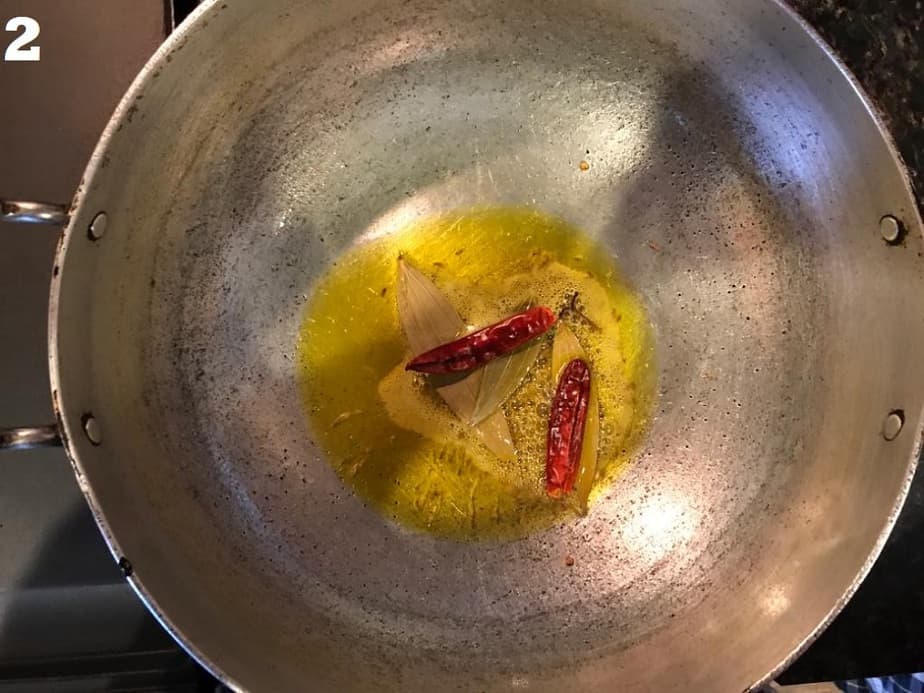 tempering oil in a kadai with cumin, red chilies and bay leaves