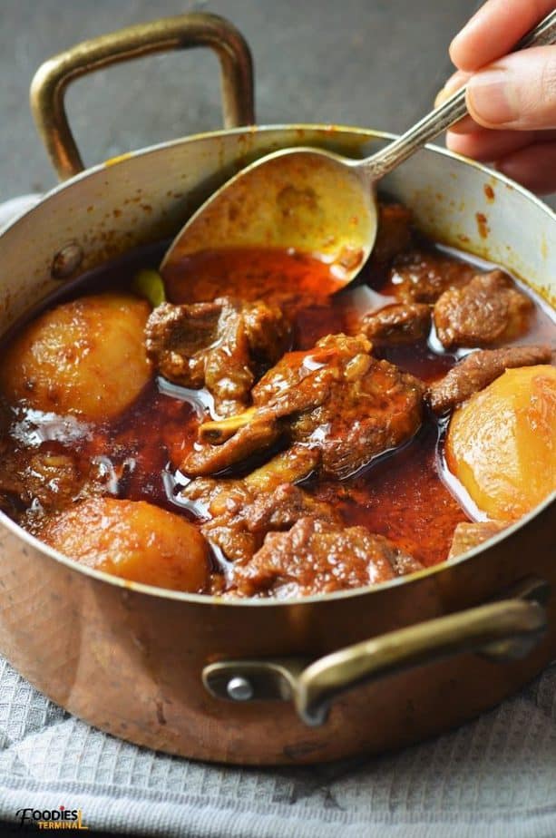 Aloo Gosht served in a copper pot with brass handles and a spoon