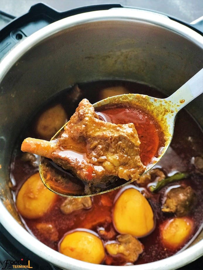 Aloo Gosht piece being lifted with a laddle from instant pot