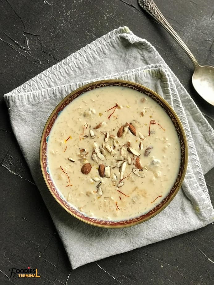 Instant Pot kheer in a brass bowl on a gray linen with a spoon beside