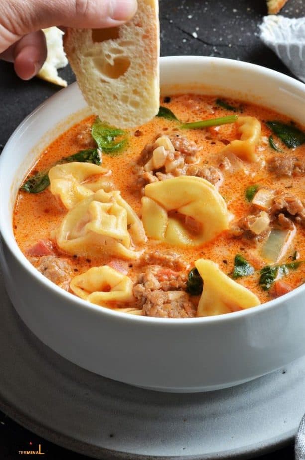 creamy sausage tortellini soup in a white bowl with a bread about to be dunked in the soup