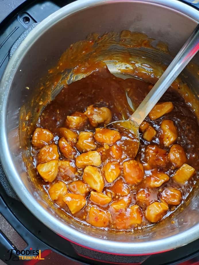 orange chicken in a sticky orange sauce inside instant pot with a steel ladle