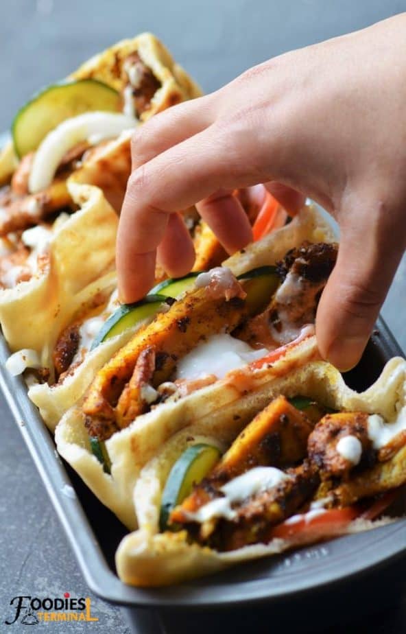instant pot chicken shawarma pita pockets with garlic sauce & veggies being lifted from a loaf tray