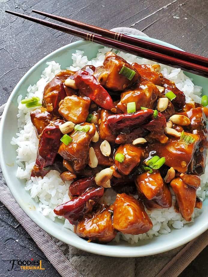 easy kung pao chicken on white rice in a light blue bowl with chopsticks