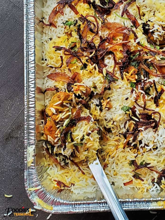 oven baked chicken dum biryani in an aluminum tray with a steel ladle