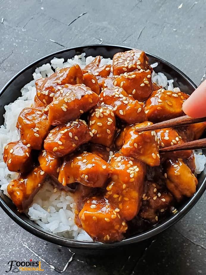 Instant Pot sesame chicken on rice in a black bowl with chopsticks