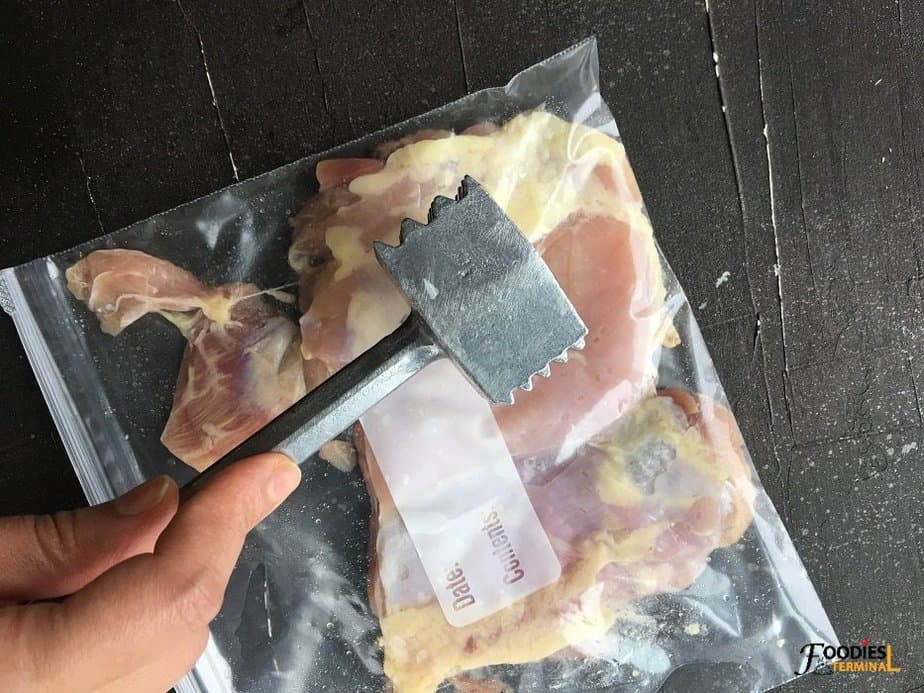 pounding chicken inside a ziplock bag with a pounder