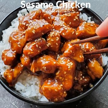 Sesame Chicken on rice in a black bowl with chopsticks