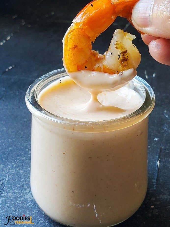 Yum Yum sauce in a small transparent glass jar with a shrimp being dipped in & lifted