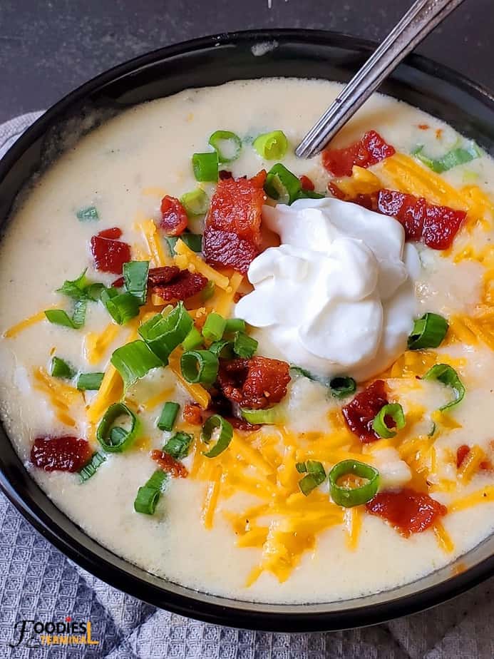 instant pot cheesy potato soup in a black bowl topped with cheddar, scallions, bacon bits & sour cream.