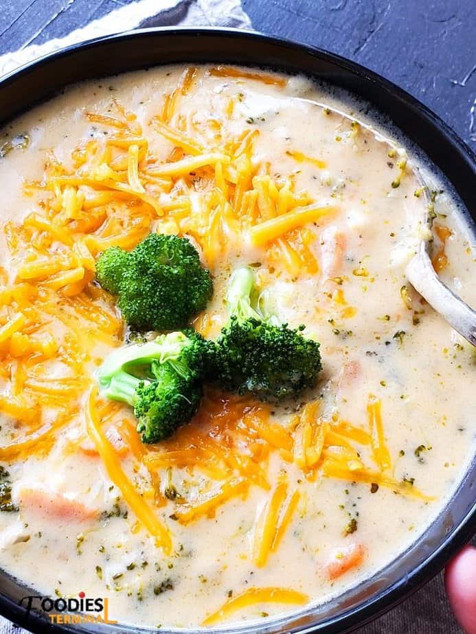 broccoli cheddar soup garnished with cheese, broccoli served in a black bowl with a spoon