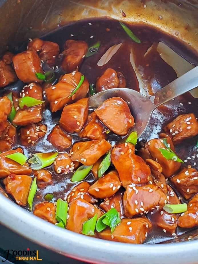 Teriyaki chicken in instant pot with a ladle and garnished with white sesame seeds and scallions
