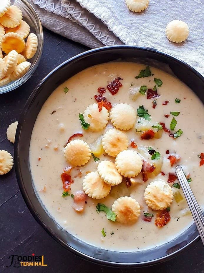 Clam Chowder served in a black bowl topped with oyster crackers, crispy fried bacon & chopped parsley