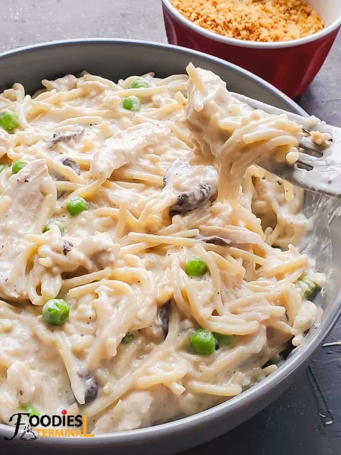 chicken tetrazzini instant pot being lifted with a fork from a grey bowl in the back ground there's a red bowl containing toasted bread crumbs