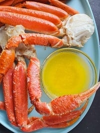butter sauce in a clear small bowl on a light blue plate with steamed snow crab clusters