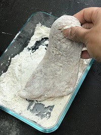 dredging chicken cutlet with flour in a glass rectangular container