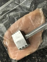 pounding chicken inside a zip lock bag with a metal pounder