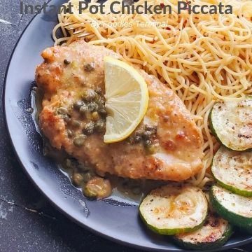 chicken piccata on a black plate with piccata sauce, lemon, noodles & zucchini