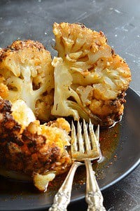 sliced whole roasted cauliflower in a black plate with forks