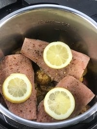 seasoned frozen salmon with lemon slices on top in the instant pot on a bed of baby potatoes