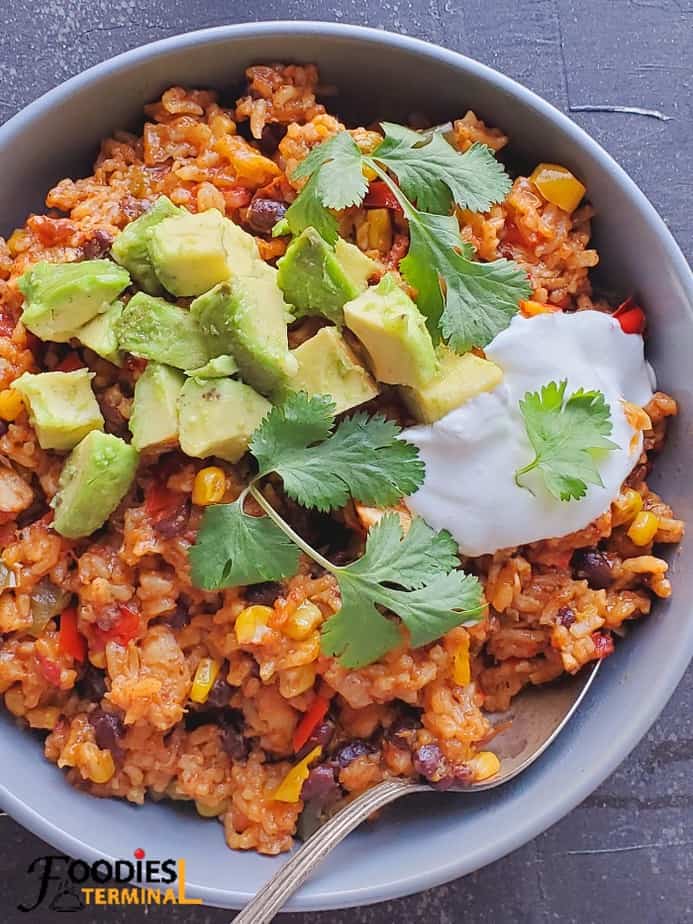 instant pot chicken fajita rice bowl in a grey bowl with spoon served with avocados, sour cream and cilantro