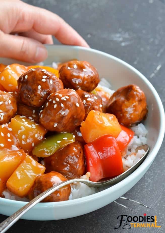sweet and sour frozen meatballs in a light blue bowl on a bed of white rice with a spoon