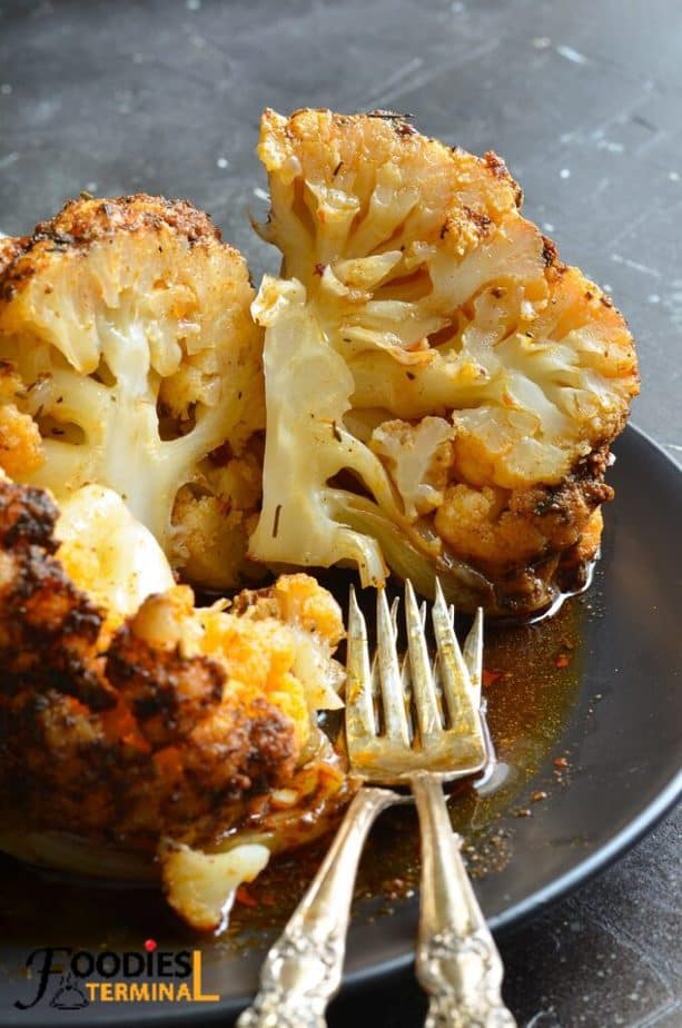 whole roasted cauliflower made in instant pot sliced and served on a black plate with forks