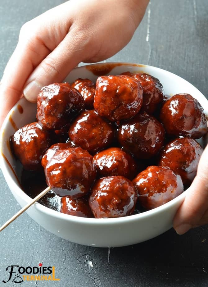 holding a white bowl containing bbq sauce grape jelly meatballs with both hands