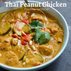 Thai Peanut butter chicken curry in a light blue plate with a spoon & garnished with cilantro & roasted peanuts