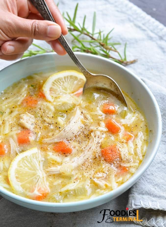 lemon chicken orzo soup garnished with lemon & ground black pepper, a spoon being dipped in the soup