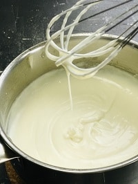 dripping stove top roux from a hand whisk into a saucepan full of roux