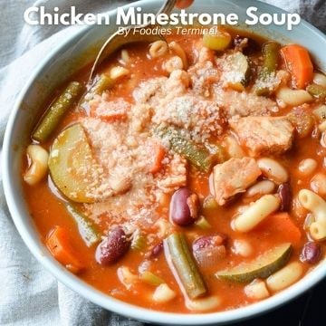 chicken minestrone soup in a bowl served with grated parmesan cheese & a spoon