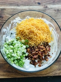 crispy bacon, cheddar, green onion added to the potato dressing mixture in a bowl