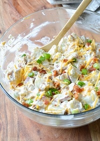 loaded baked potato salad in a clear bowl with a wooden spoon
