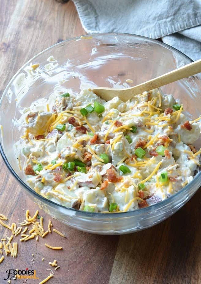 loaded baked potato salad in a clear large bowl with a wooden spoon